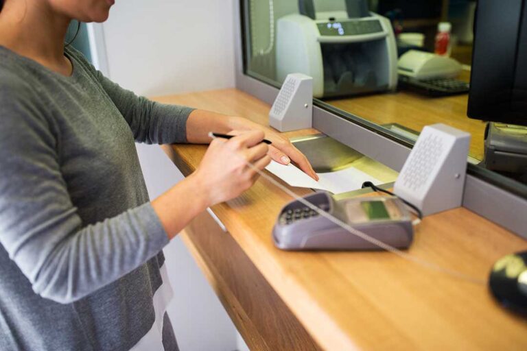 A senior couple sits at a kitchen table reviewing finances together with a calculator and paperwork.