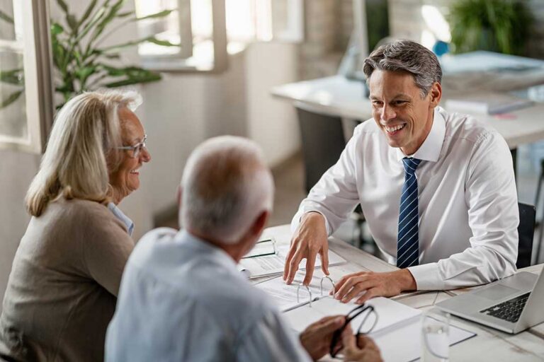 Retired couple reviewing bills, savings records, and a calculator at a kitchen table.